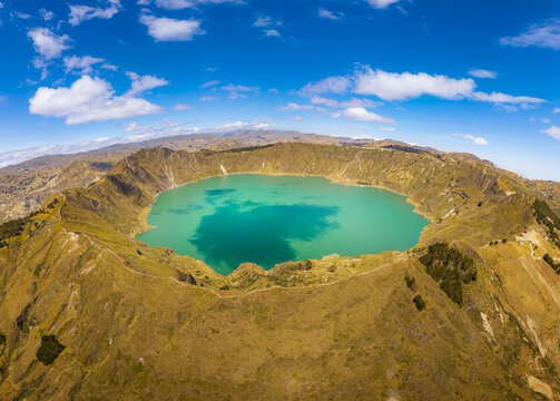 Aerial view of Quilotoa Lake, a vibrant turquoise volcanic crater lake surrounded by rugged arid slopes and distant mountains in Quilotoa, Cotopaxi, Ecuador.