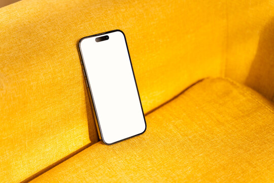 Black smartphone with blank screen on yellow sofa