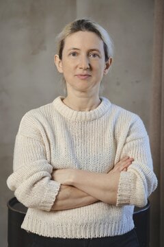 A woman poses confidently with her arms crossed, dressed in a soft, knitted sweater