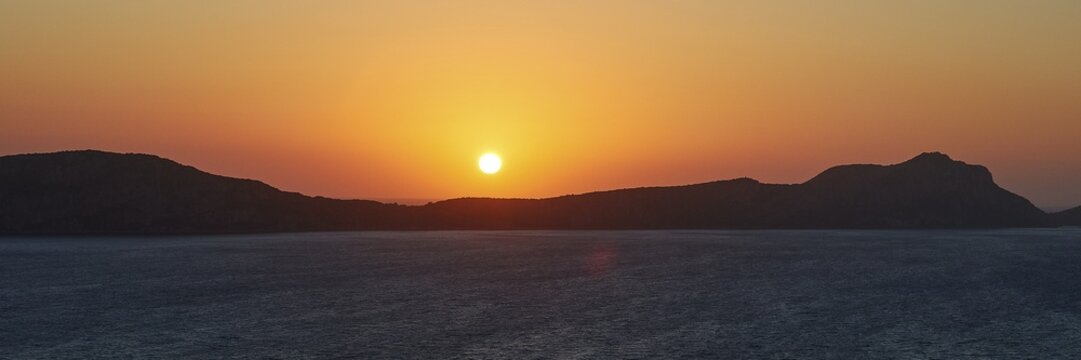 The sun sets behind a silhouette of a mountain, the sky is orange, Navarino Bay, Pylos, Peloponnese, Greece