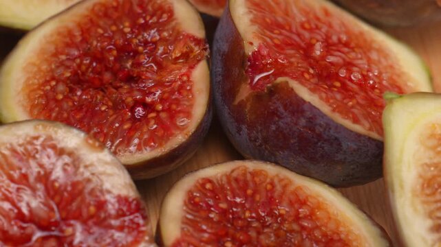 Macro shot captures ripe cut figs lying on wooden cutting board inside studio during smooth camera motion. Cinematic organic fruit video footage provides tasty textured asset for design element.