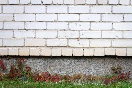 Old cracked white brick wall with green grass. Architectural detail background.