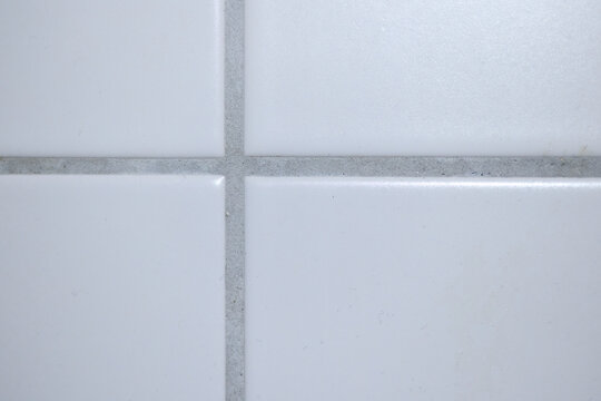 Extreme close up view of white square ceramic tile wall intersection with dark grey grout seam.