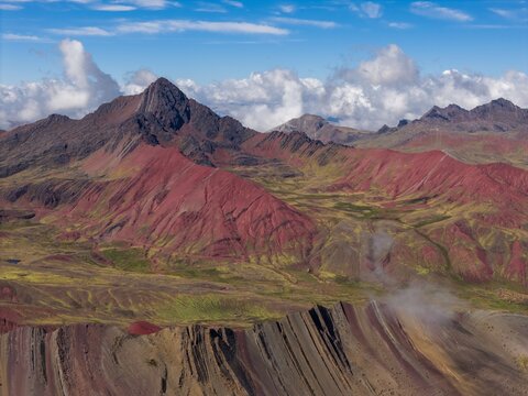 Aerial view of Vinicunca Rainbow Mountain showcasing vibrant mineral-rich slopes, rugged Andean terrain, and dramatic cloud formations in Cusco, Cuzco, Peru.