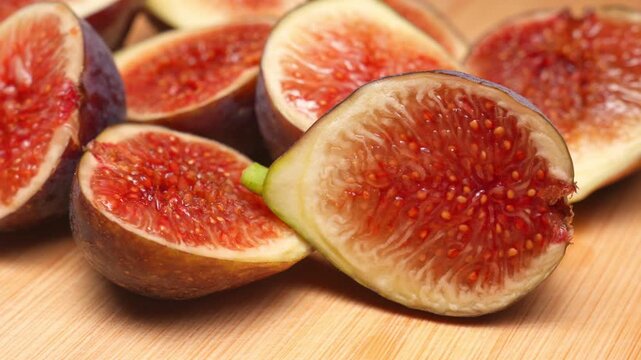 Macro shot captures ripe cut figs lying on wooden cutting board inside studio during smooth camera motion. Cinematic organic fruit video footage provides tasty textured asset for design element.