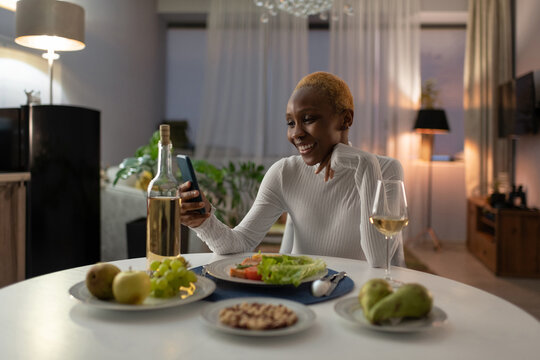 Black woman having dinner and making video call on smartphone at home