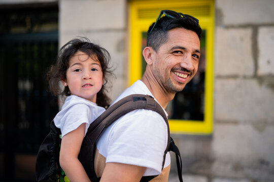 Father carrying daughter in child carrier smiling outdoors