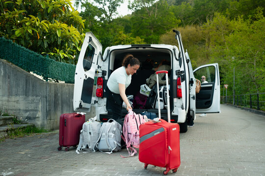Woman packing luggage into car trunk