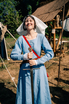 Person in Blue Dress Stands With Sword at a Medieval Festival