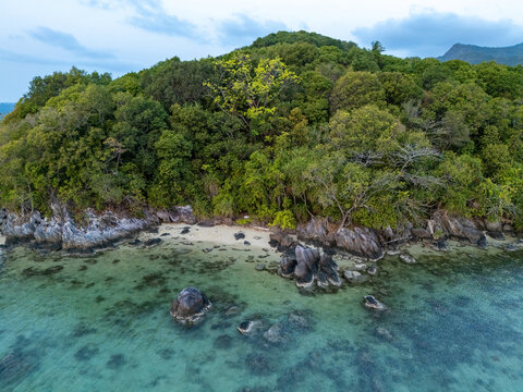 Aerial view of a lush tropical island coastline with dense green forest, rocky outcrops, and clear turquoise water in Karimunjawa, Central Java, Indonesia.