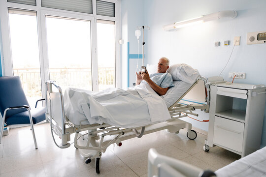 Senior male patient relaxing in hospital bed using smartphone