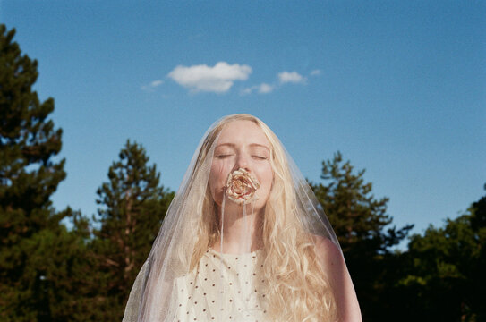 Woman With a Veil and a Rose in Her Mouth Stands Outdoors