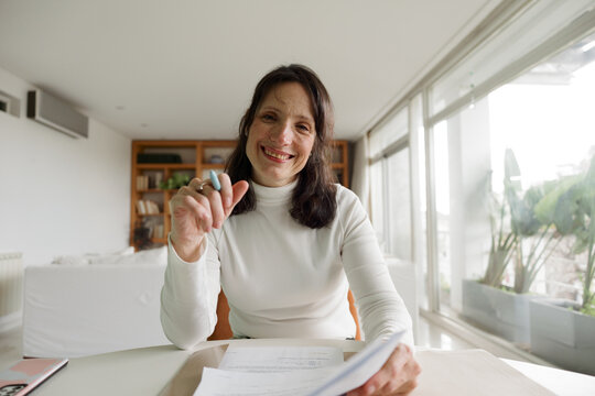 Woman Sits at a Table Smiling While Holding Papers in Her Hand
