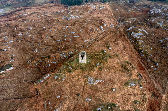 Aerial view of a historic stone ruin standing solitary on a rugged, grassy hillside with rocky outcrops in Kincasslagh, County Donegal, Ireland.