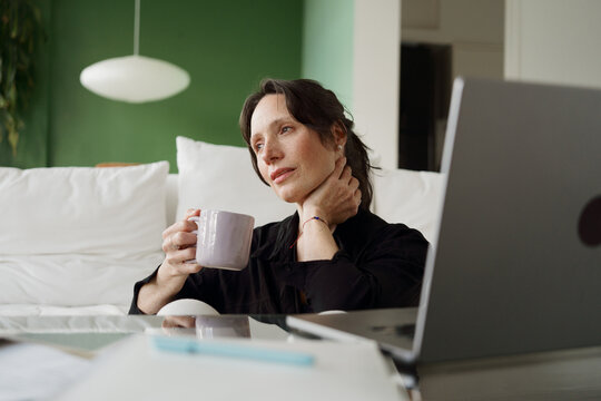 Enjoying a Cup of Coffee at Home While Working on a Laptop