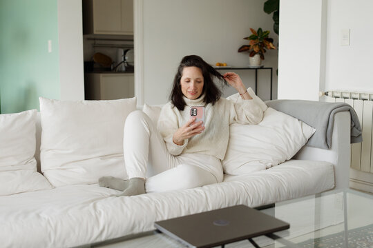 Woman Sitting on Couch Using Smartphone in Modern Living Room