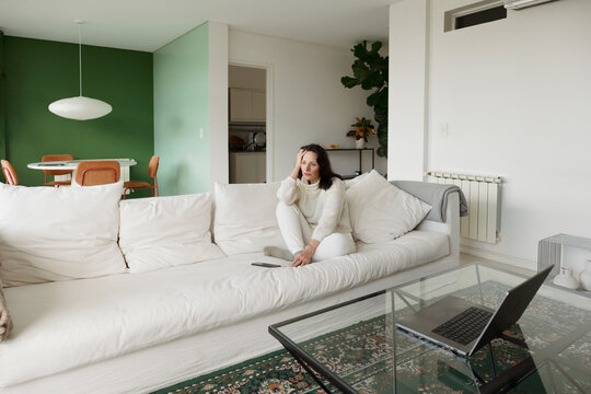 Woman Sits on Couch and Looks at Laptop in Modern Living Room