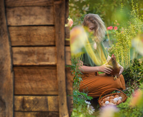 Young female farmer standing near the wooden wall of the chicken coop and holding a chicken in her hands © lesichkadesign
