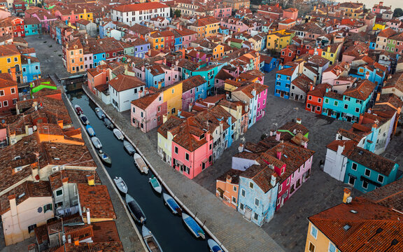 Aerial view of Burano with its iconic brightly colored houses lining the narrow canal, featuring small boats moored along the water in Venice, Veneto, Italy.