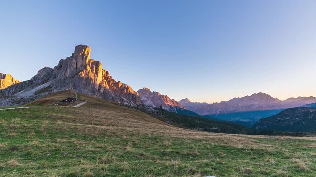 Time lapse of golden sunrise light on Ra Gusela peak at Passo Giau, Dolomites, Italy. Shadows creep across an alpine meadow under a clear sky. Serenity, passing time and freedom in the mountains