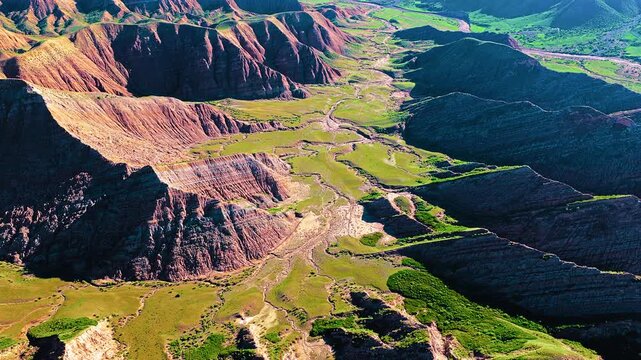 High-angle view reveals colorful layered rock formations and lush green valleys in Xinjiang Baili Danxia, captured during daytime.