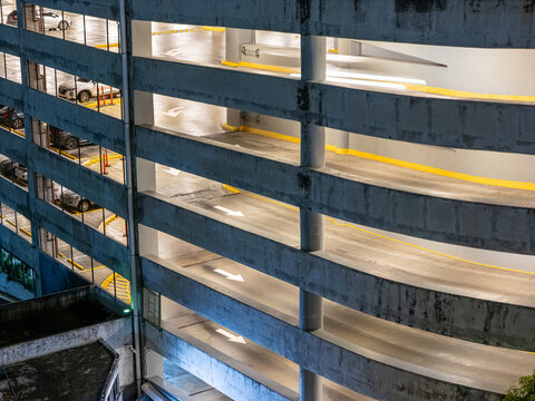 Aerial view of a multi-level concrete parking garage ramp with directional arrows and parked cars at night in Santo Domingo, Distrito Nacional, Dominican Republic.