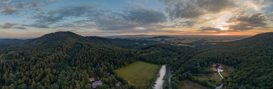 Aerial view of Przelecz Tapadla surrounded by dense forests and rolling hills under a golden sunset sky in Sobotka, Dolnoslaskie Voivodeship, Poland.