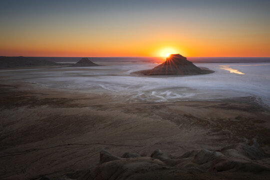 Sunset sunstar over a lone butte rising from a desert salt flat in Mangystau, Kazakhstan
