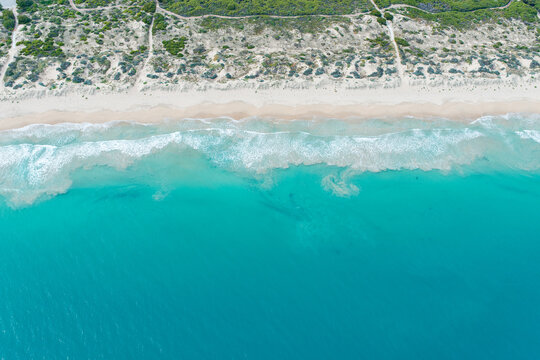 Aerial view of the pristine coastline with turquoise ocean waves crashing onto sandy beaches and dunes in Perth, Western Australia, Australia.