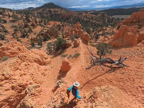 Aerial view of a woman hiking on the Arches Trail in Casto Canyon, surrounded by red rock formations and rugged terrain in Bryce Canyon City, Utah, United States.