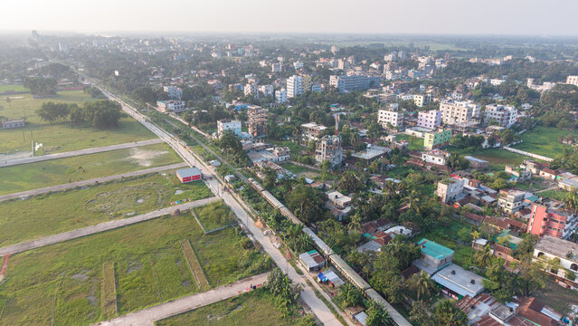Aerial view of a suburban landscape in bangladesh featuring a train passing through a residential area with green fields and scattered buildings