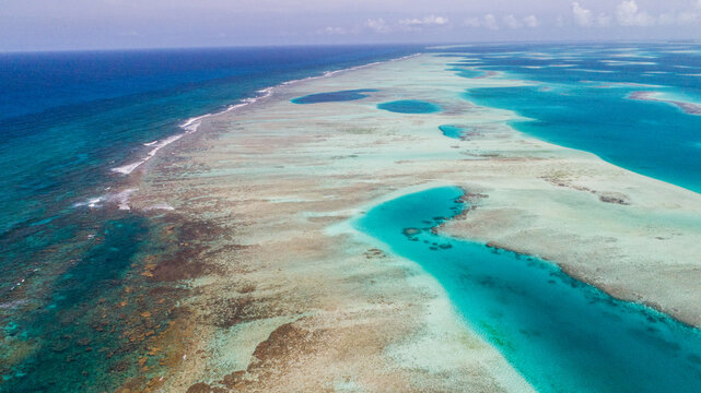 Aerial view of the Los Roques archipelago featuring vibrant turquoise waters, shallow coral reefs, and deep blue ocean expanses in Los Roques, Dependencias Federales, Venezuela.