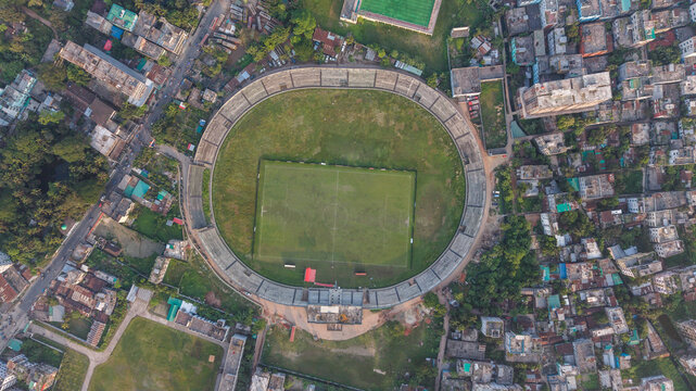 Aerial view of a circular stadium with a rectangular green field in the center, surrounded by a dense urban residential area in bangladesh