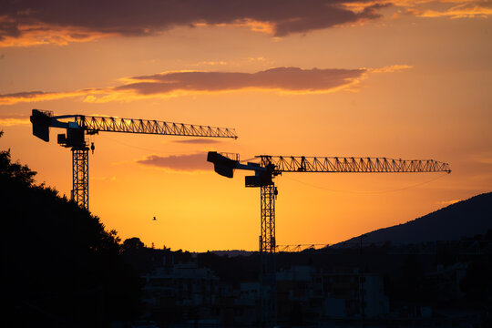View of two construction cranes silhouetted against a vibrant orange sunset sky in Nice, Provence-Alpes-Cote d'Azur, France.