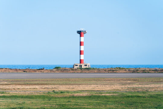 View of a red and white striped lighthouse beacon near the airport runway with the sea in the background in Nice, Provence-Alpes-Cote d'Azur, France.