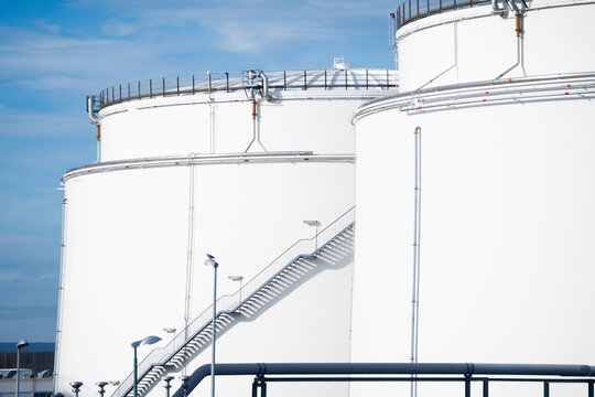 View of large white industrial storage tanks with metal staircases and piping at Frankfurt Airport in Frankfurt am Main, Hessen, Germany.