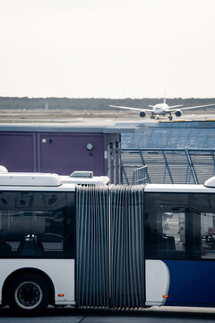 View of an airport shuttle bus parked on the tarmac with an airplane taxiing on the runway in the background at Frankfurt Airport in Frankfurt am Main, Hessen, Germany.