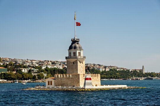 View of the historic Maiden's Tower on a small islet in the Bosphorus, featuring stone architecture, a Turkish flag, and the coastal cityscape of Uskudar, Istanbul, Turkey.