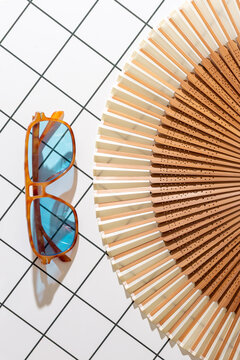 Sunglasses and folding fan on a white surface