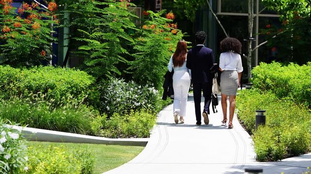 Three colleagues seen from behind as they walk deeper into a green office garden, an unobtrusive back view that suits corporate, ESG and recruitment voiceovers and captions