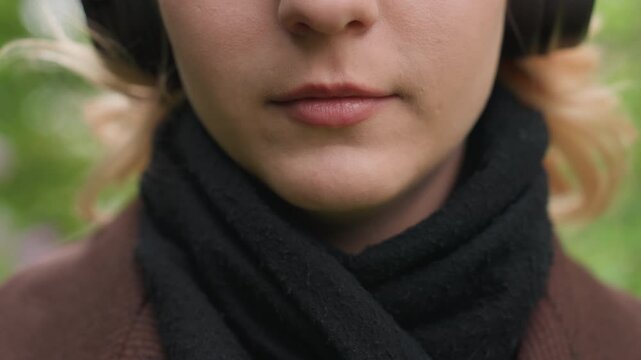 Close up shot focuses on woman lower face and neck. Woman wears black scarf wrapped around her neck paired with brown top. background is softly blurred green foliage