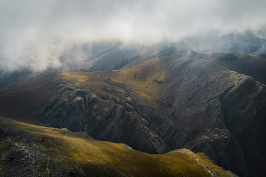 View of rugged mountain slopes with rocky textures and patches of golden grass partially obscured by low-hanging clouds in Sierra de La Ventana, Buenos Aires Province, Argentina.