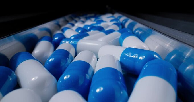 Tracking shot of blue and white capsules rolling along pharmaceutical conveyor belt in production line on manufacturing.