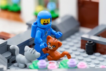 Obraz premium Tambov, Russian Federation - September 24, 2026 A blue Lego astronaut minifigure interactively bends down toward a ginger cat and a gray cat outdoors.