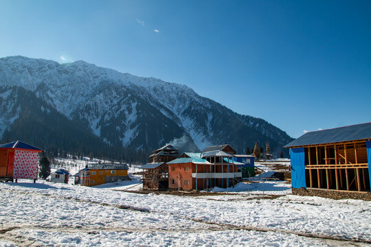 View of Arang Kel village with colorful wooden houses nestled in a snow-covered mountain landscape under a clear blue sky in Arang Kel, Kashmir, Pakistan.