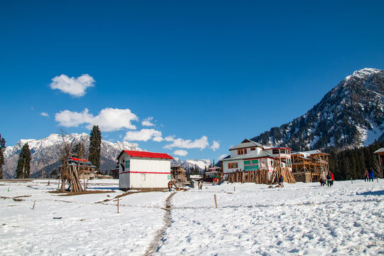 View of Arang Kel village with wooden houses set against snow-covered mountains under a clear blue sky in Arang Kel, Kashmir, Pakistan.