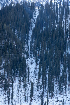 View of the cable car suspended over a steep, snow-covered mountain slope with dense pine trees in Arang Kel, Kashmir, Pakistan.