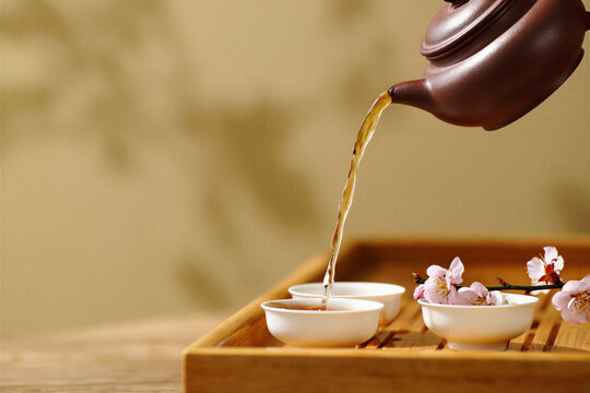 Clay teapot pouring amber tea into porcelain cups on a tray
