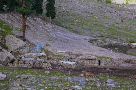 View of traditional stone huts with smoke rising from a chimney in the rugged landscape of Rama Meadows, Astore, Gilgit, Pakistan.