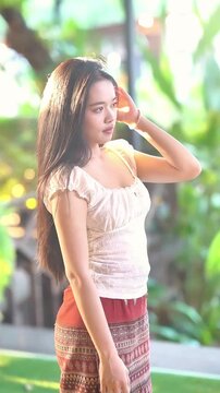 Slow motion of a beautiful Asian woman in traditional Thai attire posing gracefully outdoors.
